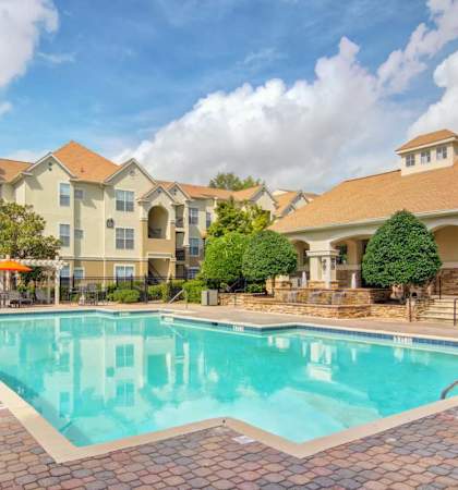 A large swimming pool in front of a building with a patio and umbrellas.