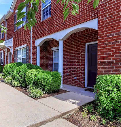 A row of red brick houses with green bushes in front.