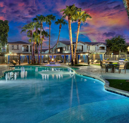A swimming pool surrounded by palm trees and a house in the background.