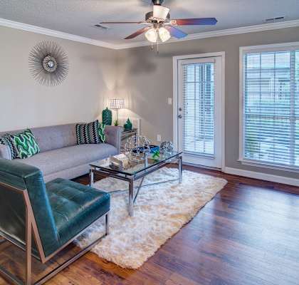 A living room with a grey couch, a green chair, and a glass coffee table at Huntington Chase Apartments, Warner Robins, GA