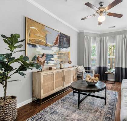 A living room with a ceiling fan, a large painting, a wooden cabinet, a coffee table, and a potted plant.