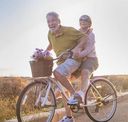 Lifestyle photo of older couple riding a bike together at Oaks at Pompano, Pompano Beach
