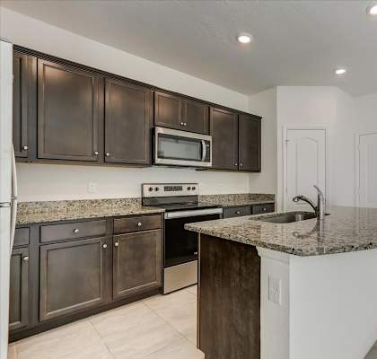 A modern kitchen features dark cabinets, a speckled granite countertop island with a sink, and stainless steel appliances against white walls.