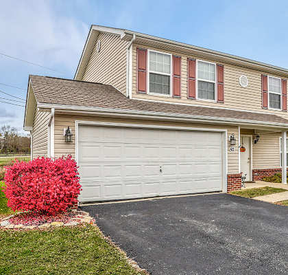 A house with a grey garage door and red bushes in front.