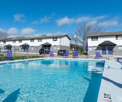A swimming pool with blue chairs and a white building in the background.