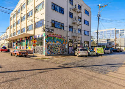 A street view of a building with graffiti on the side and cars parked in front.