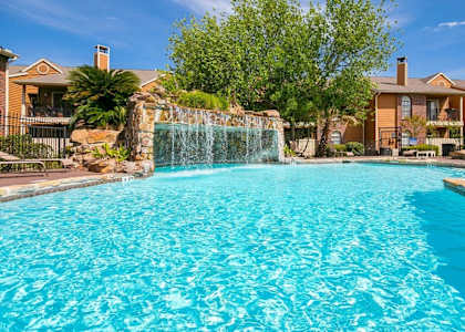 a large pool with a waterfall in front of a house at Oaks of Westlakes Apartments, San Antonio, 78245