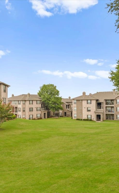 a large grassy area with apartment buildings in the background at The Clairborne Apartment Homes, Grand Prairie, TX, 75050
