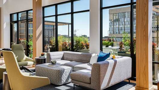 Front lounge with a yellow chair and a grey couch and large windows in the background.