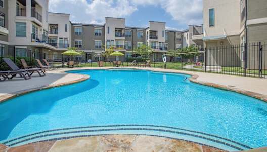 A swimming pool in a residential area surrounded by apartment buildings. at Millennium on Post Apartments, San Marcos, TX, 78666