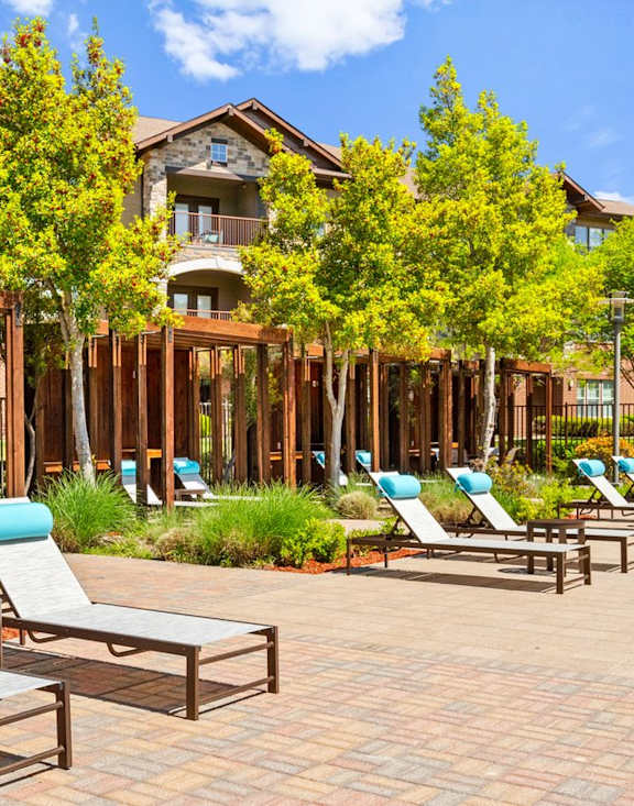 a patio with lounge chairs and tables and a building in the background