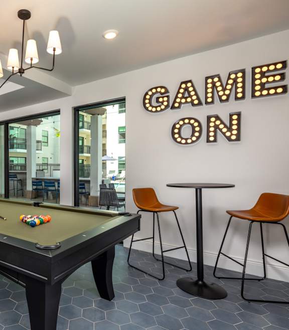 A pool table with a sign that says "Game On" behind it.
