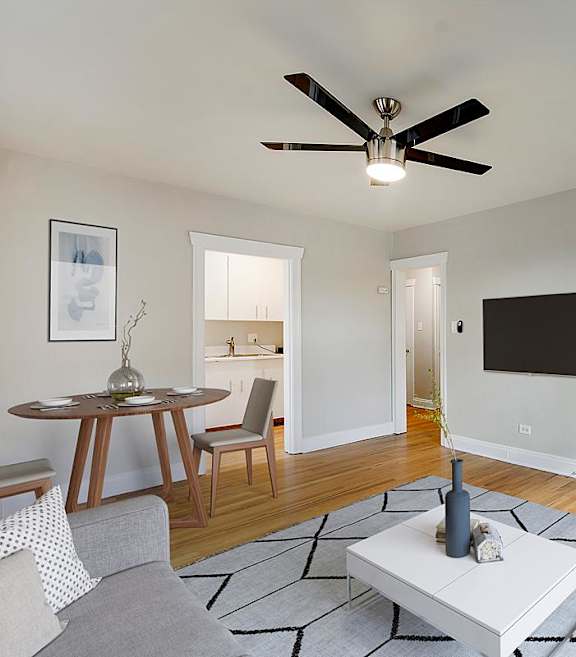 A living room with a grey sofa, a white coffee table, a ceiling fan, and a television.