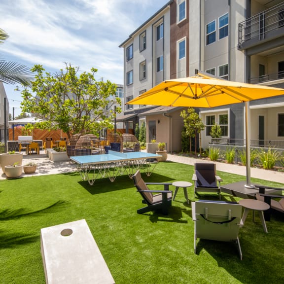 A yellow umbrella is on a lawn with chairs and a table at Citron Anaheim
