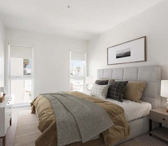 A bedroom with a bed covered in a striped comforter and a white nightstand with a lamp on it.