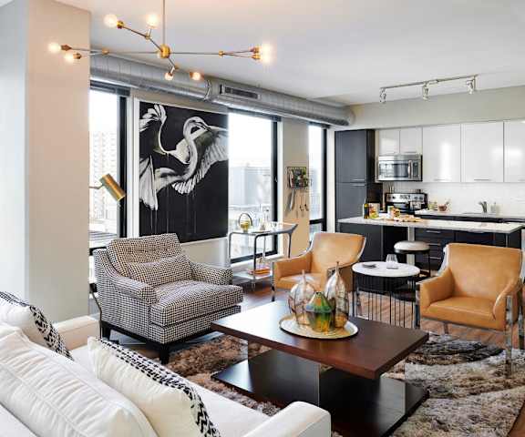 The living room at 4Marq with chairs, a couch, and a coffee table and the kitchen in the background. 