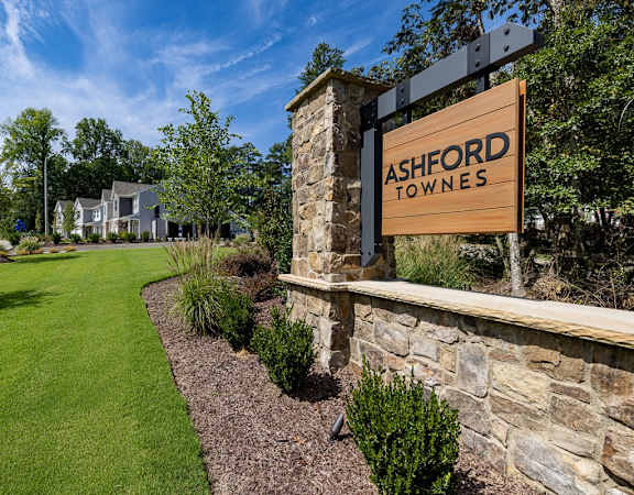 a sign for ashford towers on a stone wall next to a lawn and trees