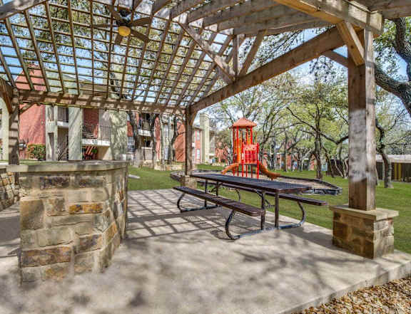 A picnic table is under a wooden pergola. at Wildwood Apartments , Austin, 78752
