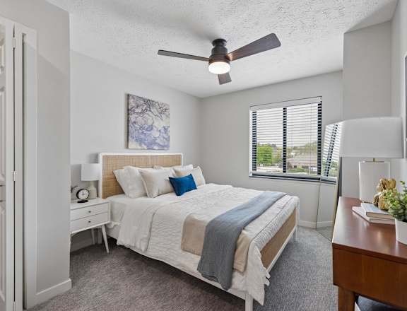 Bright apartment bedroom with ceiling fan and large window.