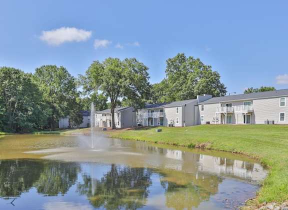 a pond with a fountain in front of a row of condominiums