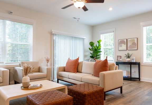 A living room with a white sofa, a brown ottoman, and a white coffee table.