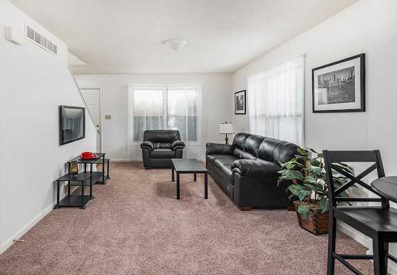A living room with a black leather couch and a black chair.