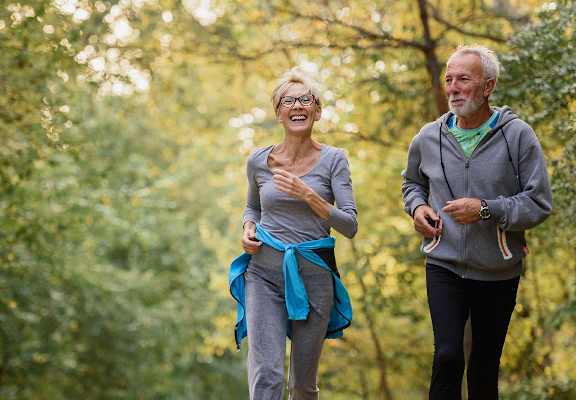 A man and a woman are jogging in a forest.