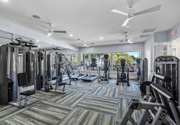 A gym with a variety of equipment including treadmills, weights, and a ceiling fan.