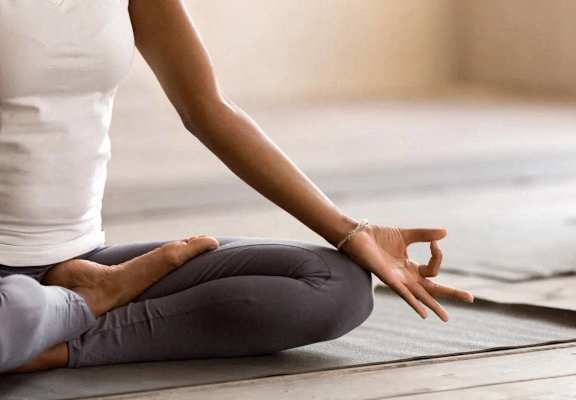 A person is sitting cross-legged on a yoga mat in a meditative pose.