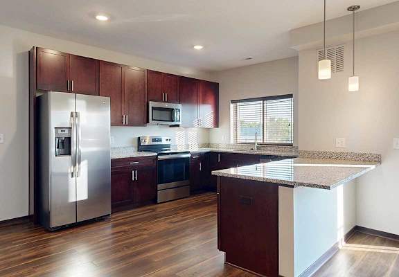 A modern kitchen with dark wooden cabinets, granite countertops, stainless steel appliances, a large window over the sink, and a peninsula counter.