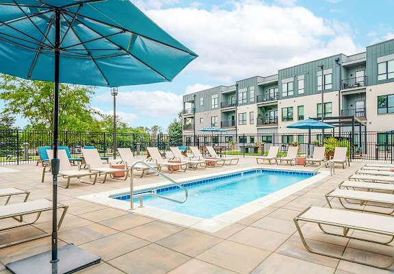 A pool surrounded by chairs and umbrellas in front of an apartment building.