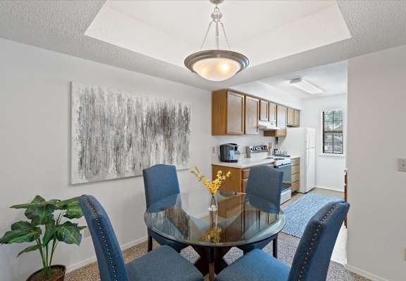a dining area with a glass table and chairs and a kitchen in the background