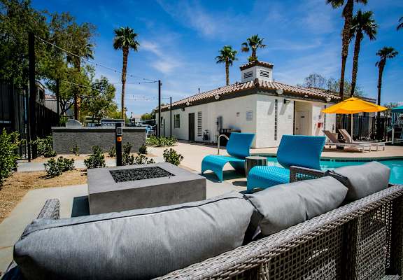 a patio with blue chairs and a fire pit in front of a white house