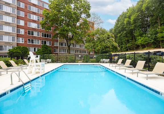 A large swimming pool with lounge chairs and a building in the background.