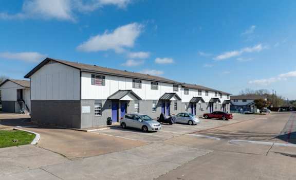 A parking lot in front of a building with cars parked.