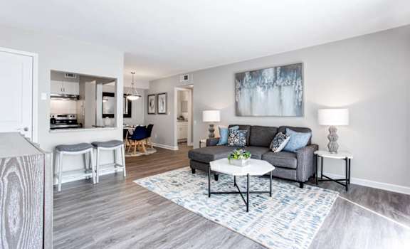 A living room with a grey couch, a white coffee table, and a painting on the wall at Barcelo at East Cobb Apartments, Marietta, GA