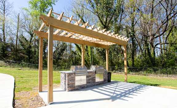 A wooden pergola structure is situated over a stone bench in a park at Barcelo at East Cobb Apartments, Georgia, 30067