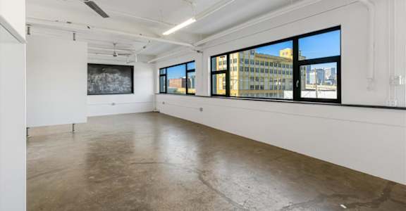 A spacious, empty room with a ceiling fan and large windows.