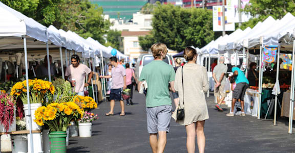 two people are walking through a farmers market