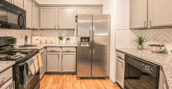 A modern kitchen with a stainless steel refrigerator and wooden floors.