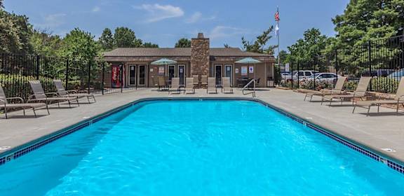 A large swimming pool surrounded by lounge chairs and a small building in the background.