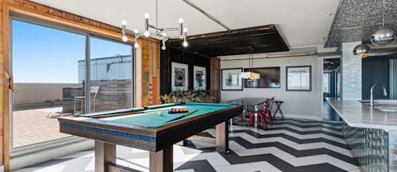 A pool table is in the middle of a room with a chevron patterned floor.