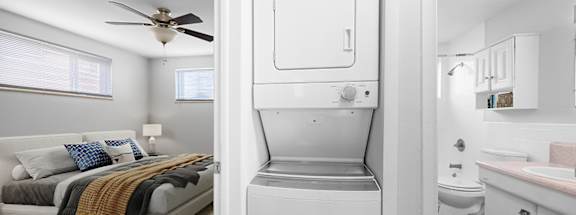 A white fridge is in the middle of a room with a bed and a bathroom.