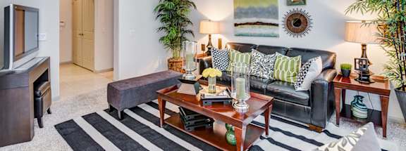 A living room with a black couch and a striped rug.