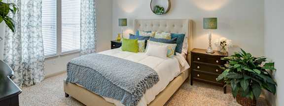 A bedroom with a bed, nightstand, and a plant.