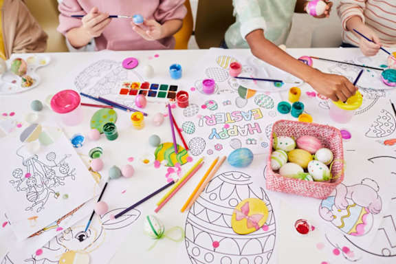Children are painting Easter eggs on a table with various art supplies.
