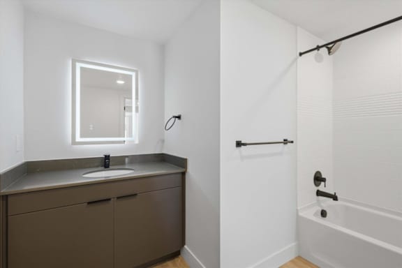 A modern bathroom with a white tub and a brown vanity at Brickside Heights, Millcreek, UT, 84106