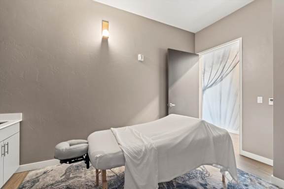 A room with a bed covered in a white sheet and a small ottoman.