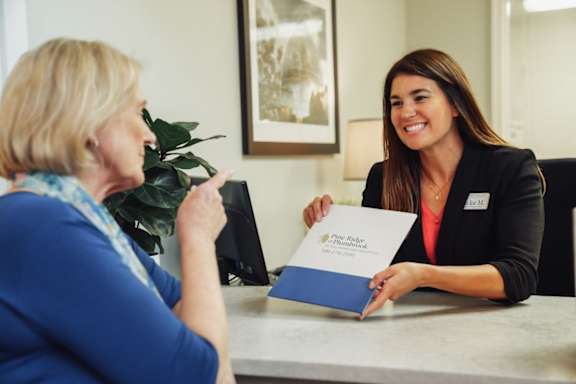 A woman in a blue shirt is sitting at a desk with a folder in front of her.