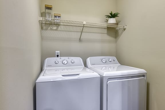 a washer and dryer in an empty laundry room with a shelf above them